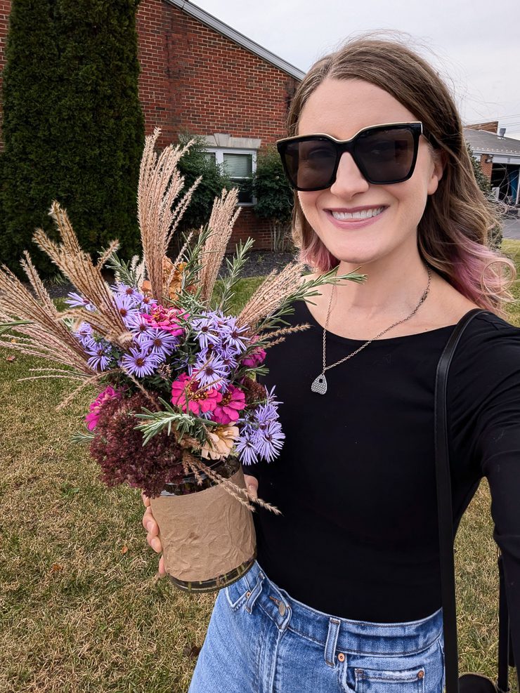 woman smiling with a fall arrangement of cut flowers