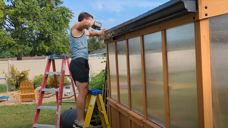 man attaching a gutter to a greenhouse