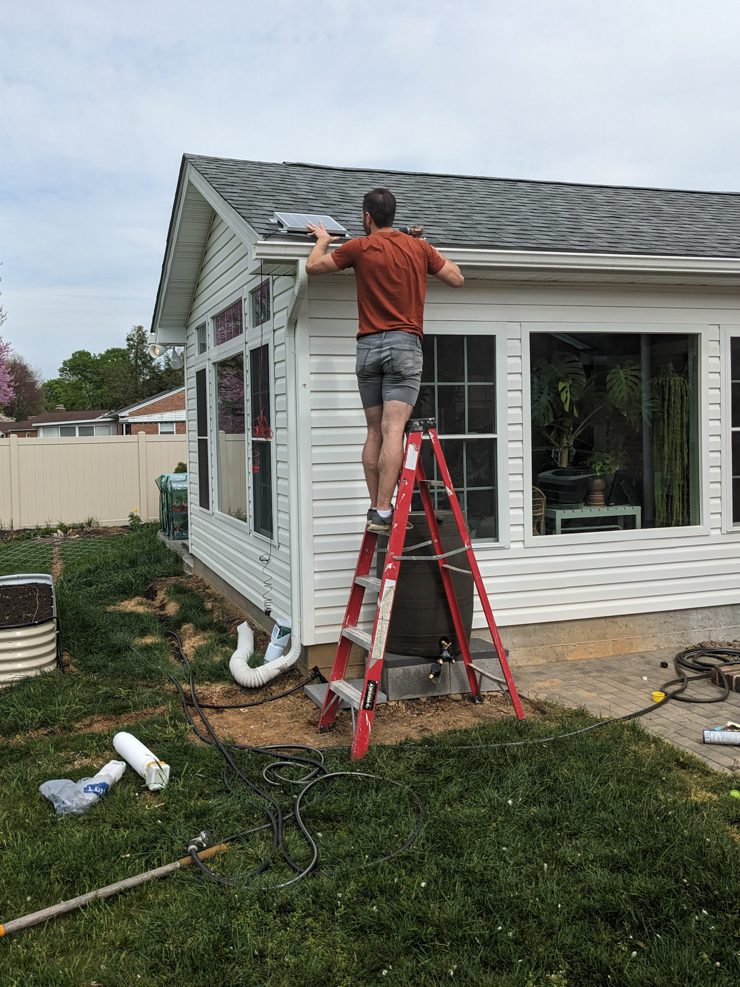man with a nice physique standing on a ladder putting a solar panel on a roof